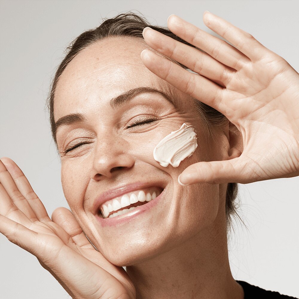 Woman smiling while applying moisturizer